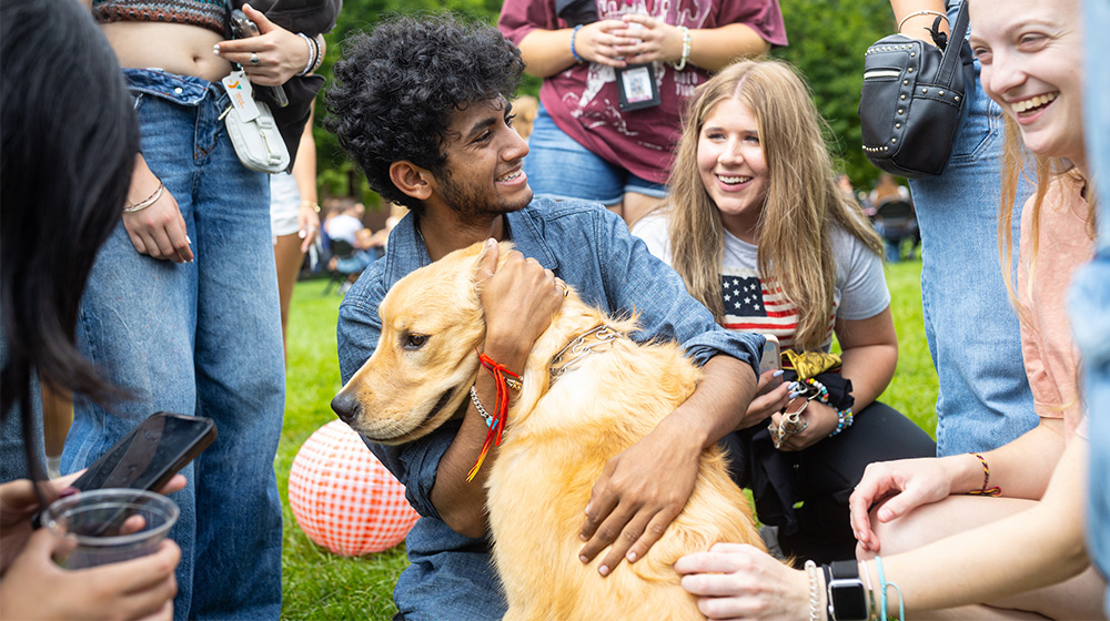 A group of students play and cuddle with Sullivan on the East Quad of Lake Shore Campus.
