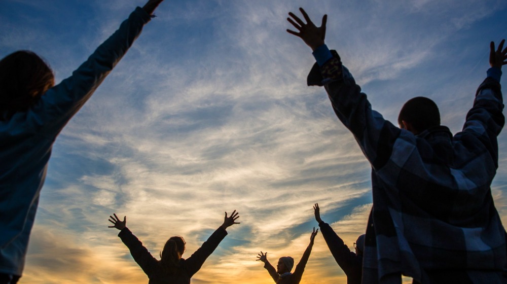 Cloudy blue sky as sun rise and 5 silhouettes with their arms in the air