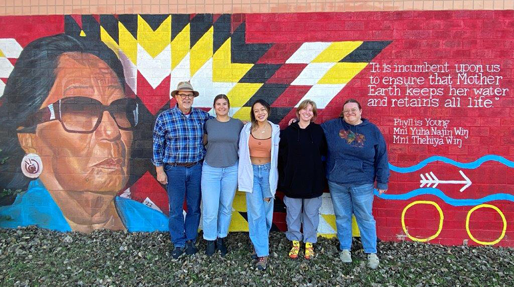 Students in front of a mural depicting Standing Rock leader Phyllis Young