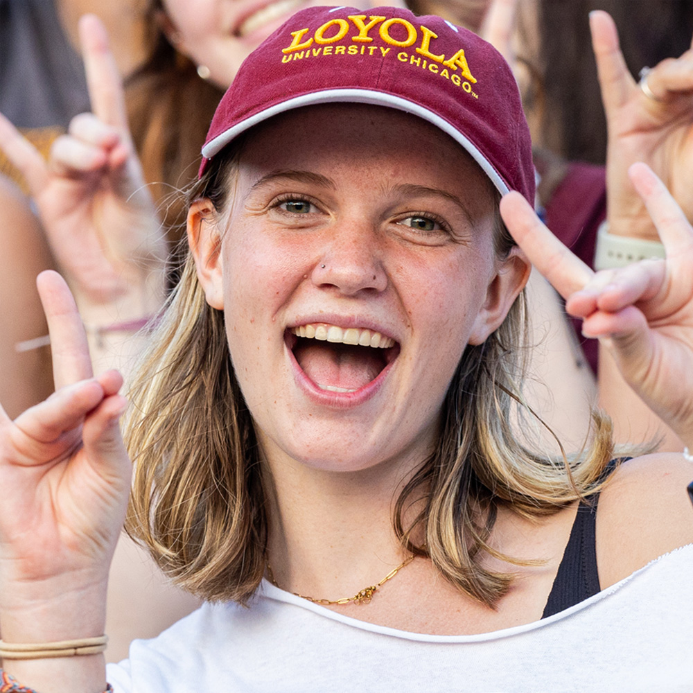A student wearing a Loyola baseball cap makes the wolf sign with her hands at an event during Welcome Week