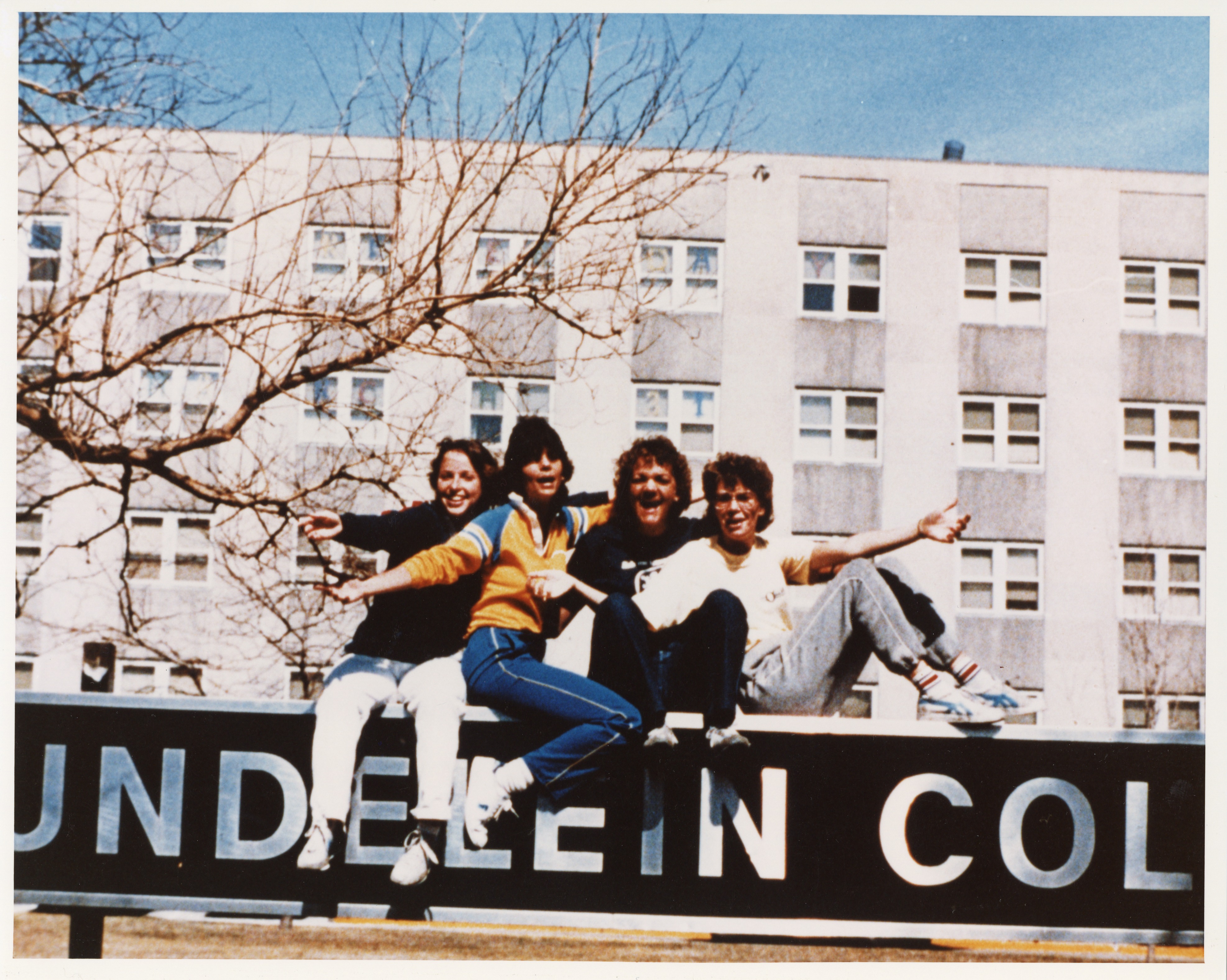 Students sit on a sign for Mundelein College outside Coffey Hall