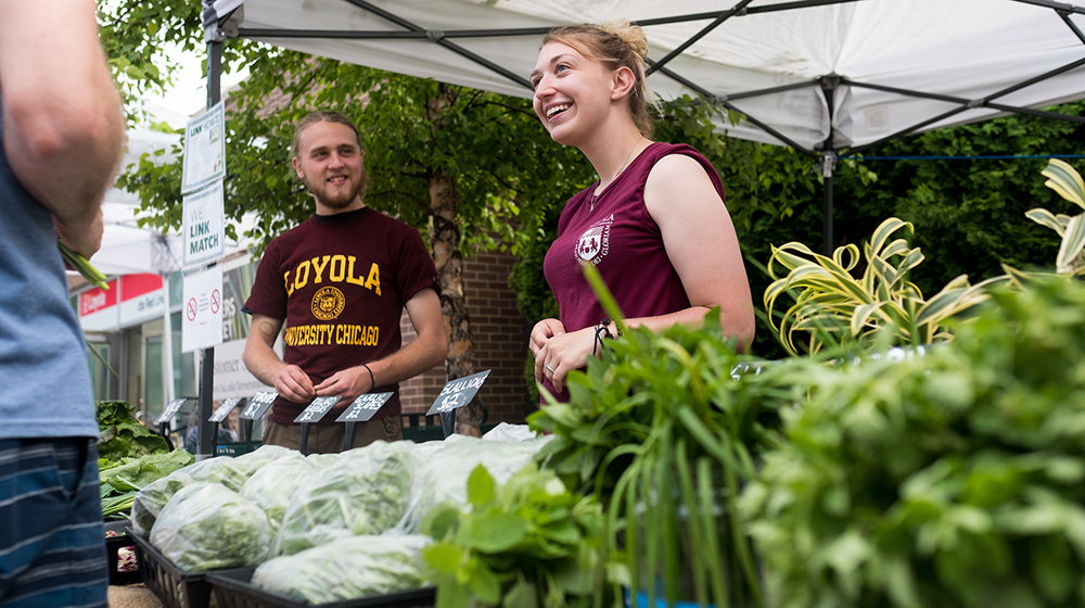 Loyola students Patrick Baranovskis and Sydney Nice—both enrolled in the School of Environmental Sustainability—help customers pick out fresh produce at the Loyola Farmer's Market on Loyola Plaza. The market gives local residents an outlet to purchase healthy, locally grown foods. (Photo: Lukas Keapproth)
