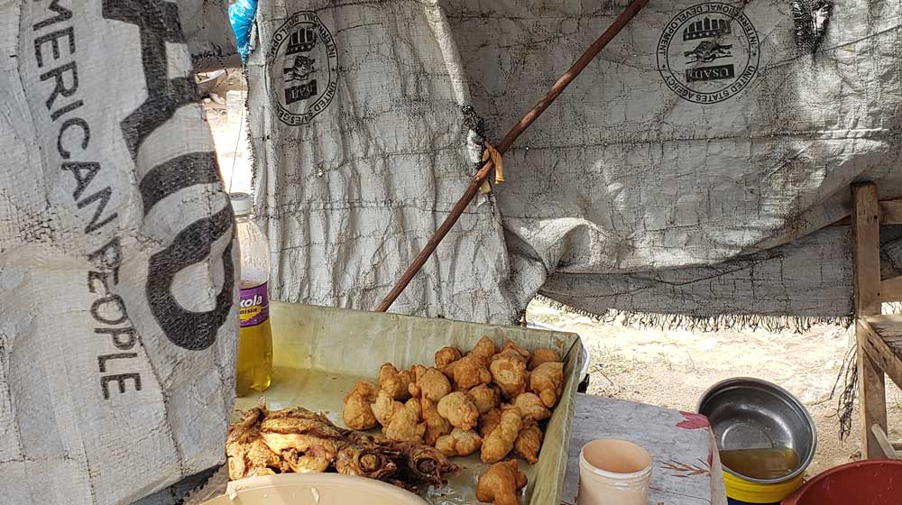 USAID banners, a rare sign of aid, are seen in southern shore Haiti, where Loyola sociology graduate student Stéphanie Jean-Baptiste spoke with people to determine the effects of Hurricane Matthew in 2019. This photo shows the only equivalent of a restaurant that was in the area, which primarily sold fried fish caught by local fishermen, fried plantain, and marinad, a type of fried salted pastry. (Photo: Stéphanie Jean-Baptiste)