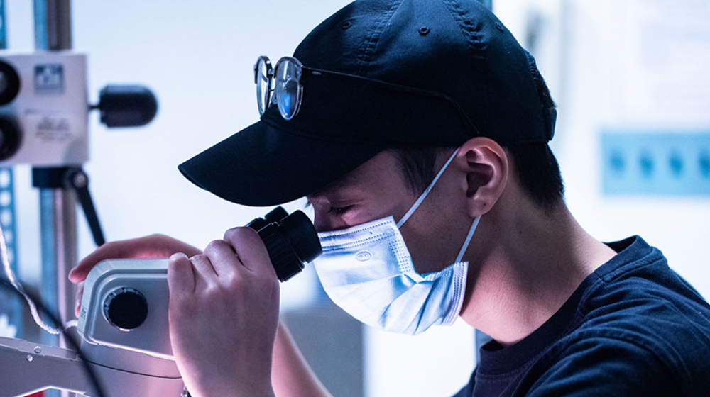 a closeup of someone wearing a mask and looking through a microscope 